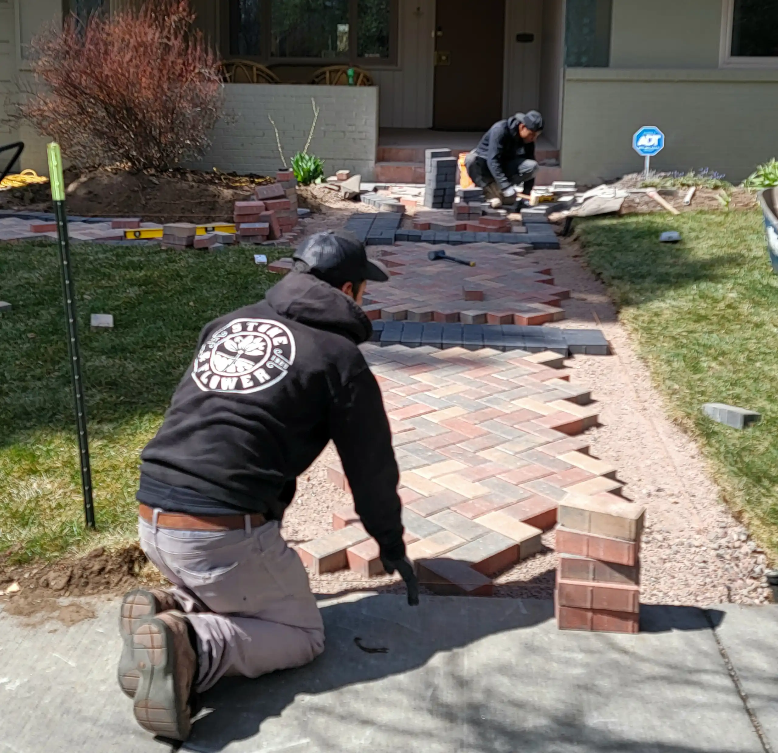 Two workers laying herringbone pattern brick pavers for a front walkway.