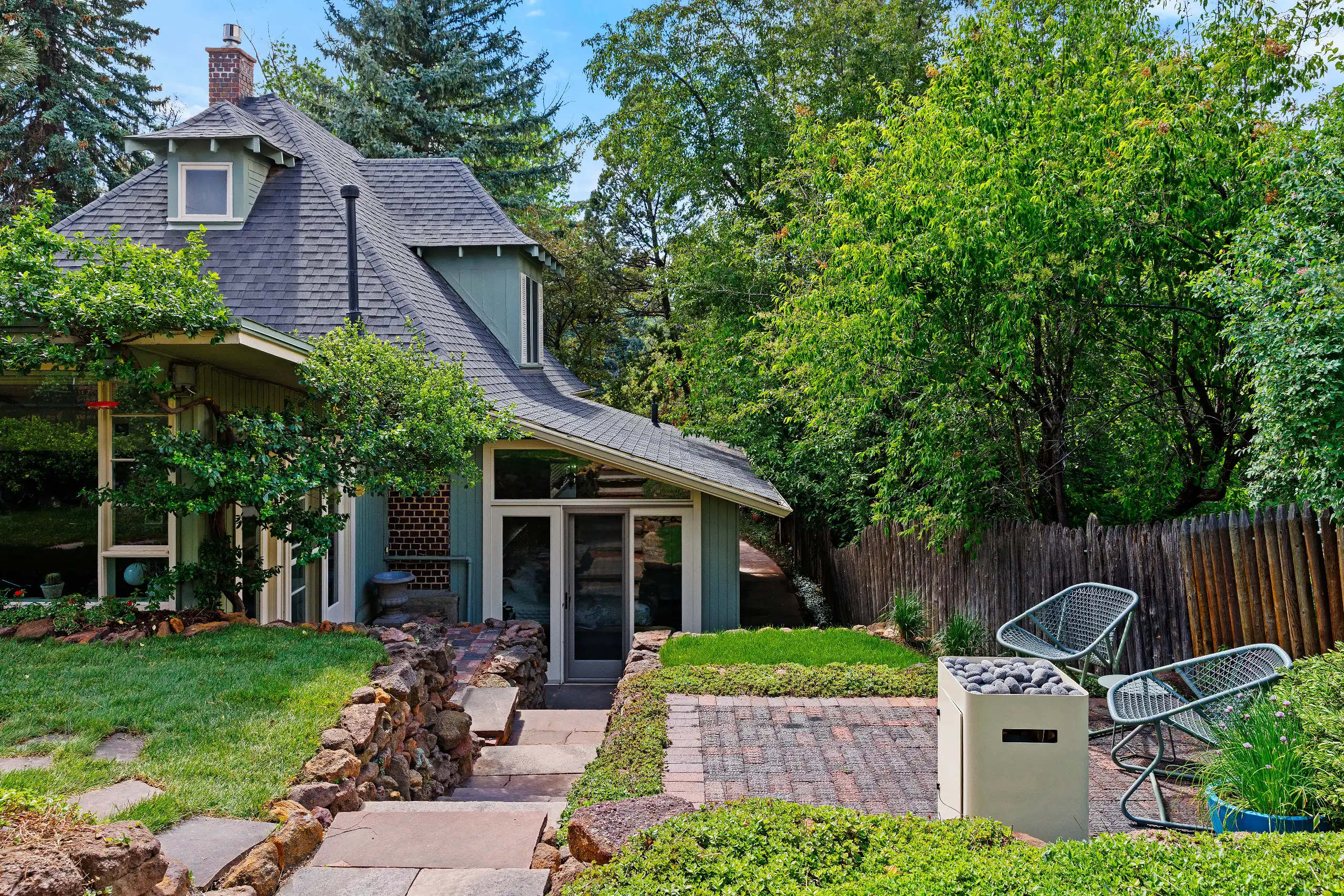 Cozy cottage house with a terraced stone patio, fire pit, and lawn chairs.