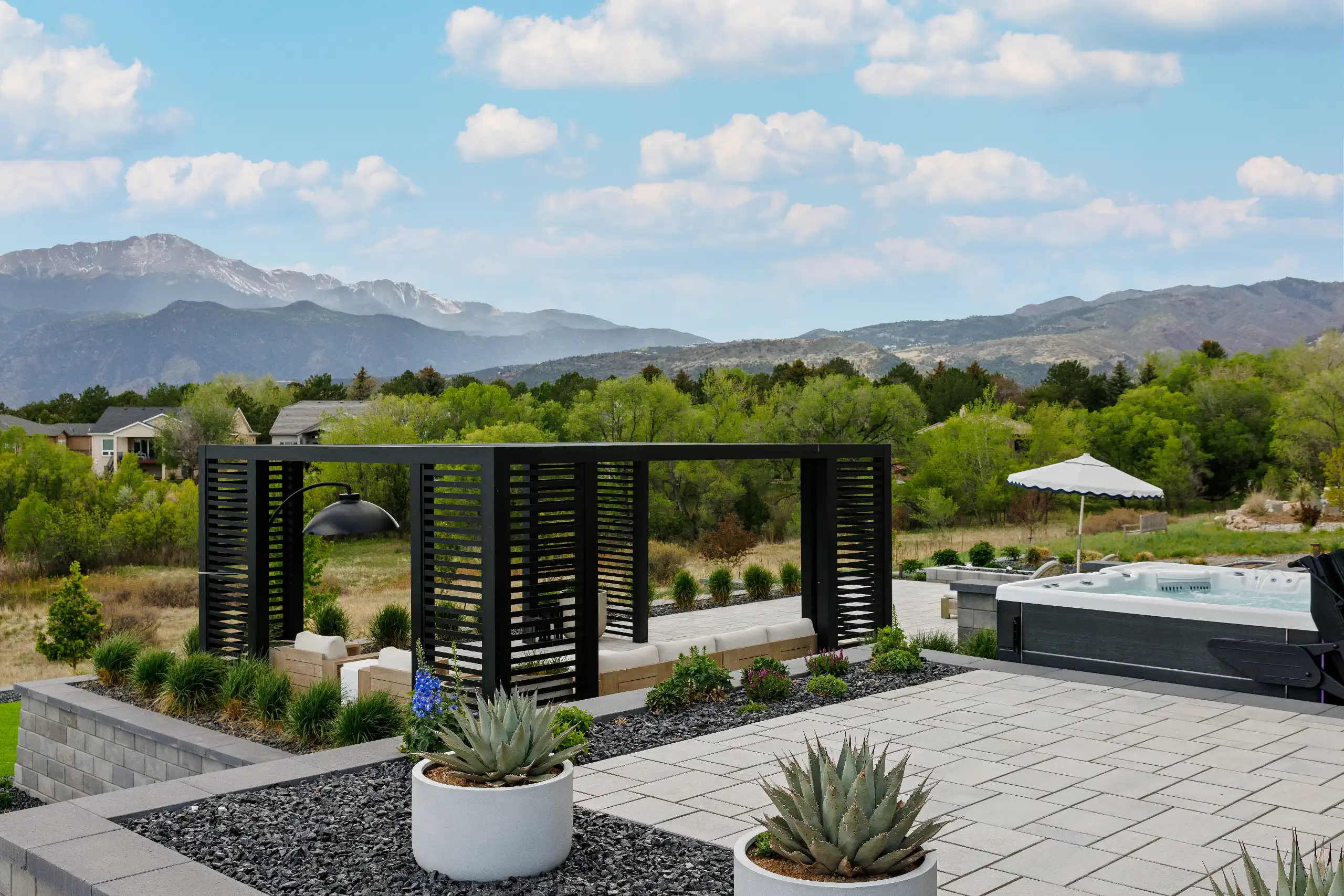 Modern tiered patio with a black pergola, hot tub, and a mountain view.