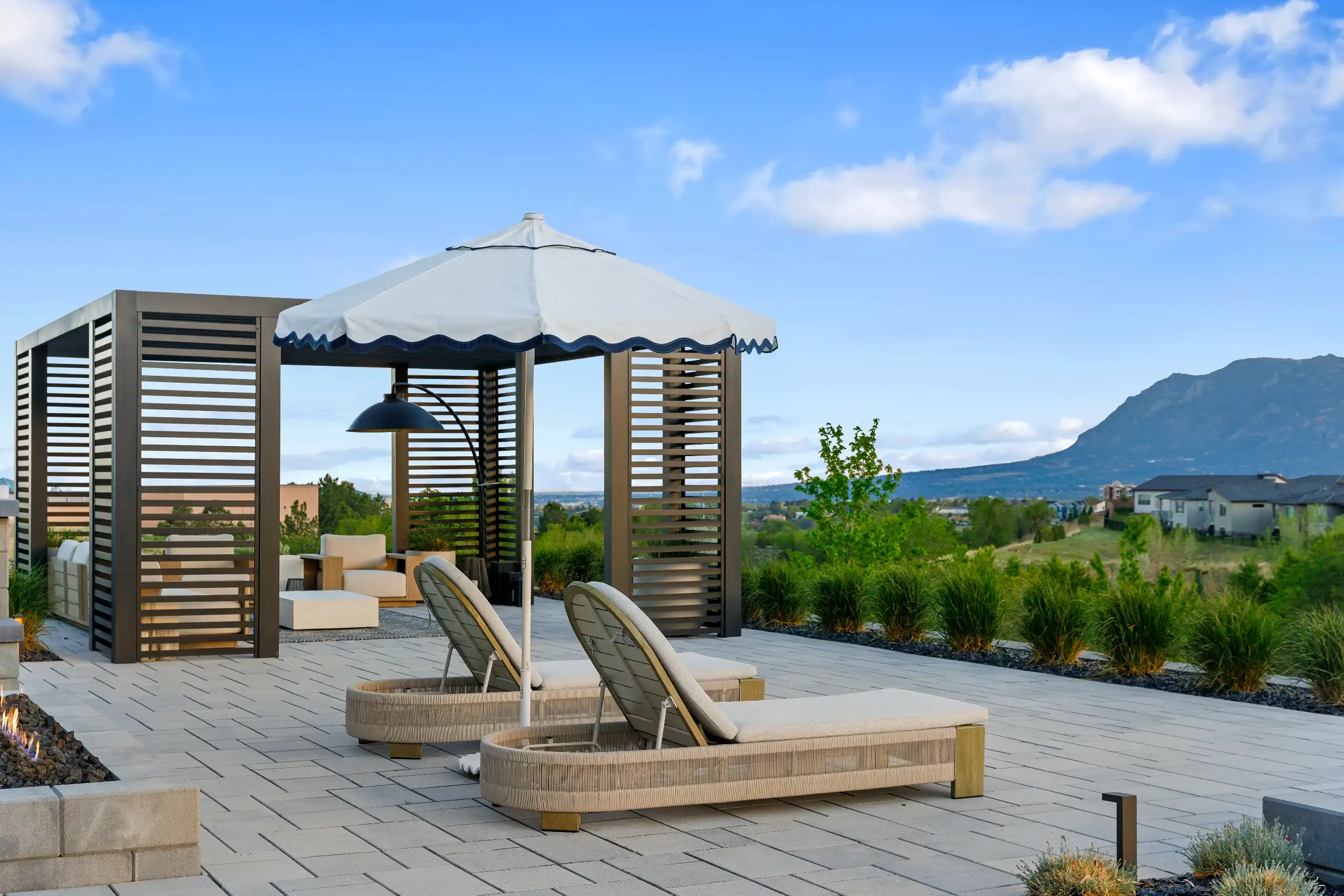 Two woven outdoor lounge chairs under a white umbrella on a stone patio