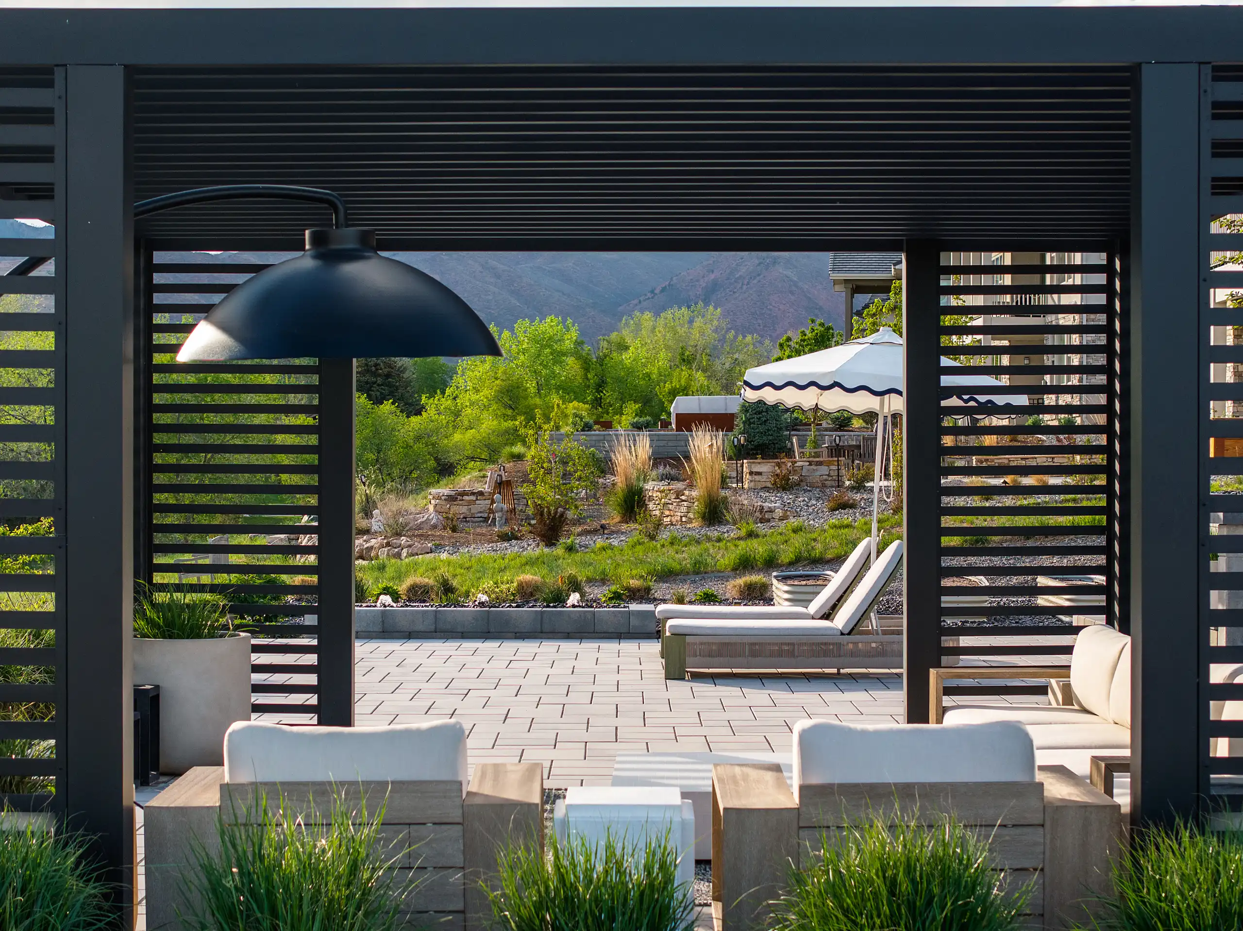 View from inside a black slatted pergola looking out toward a patio with lounge chairs