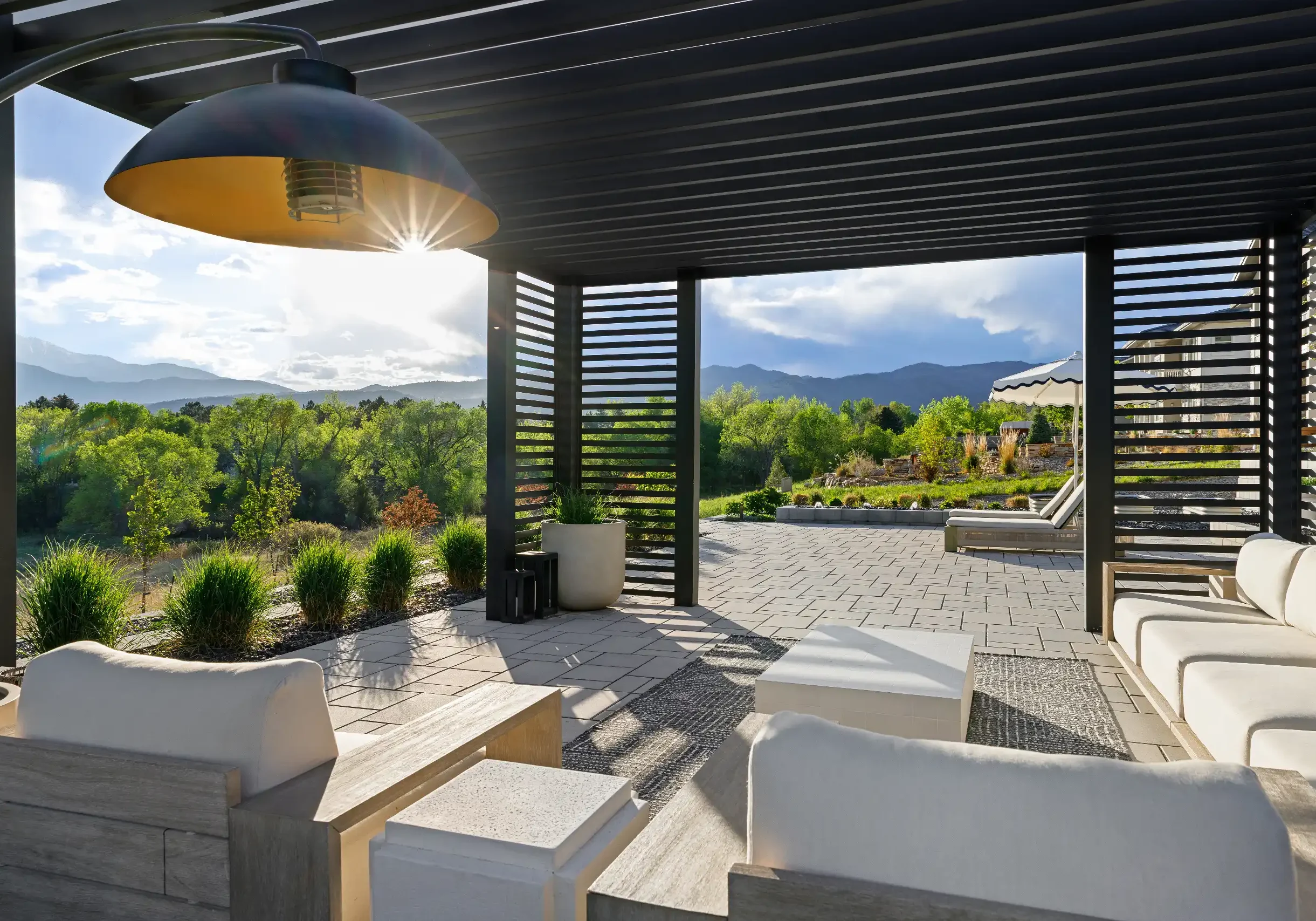 Modern outdoor lounge under a black slatted pergola overlooking distant mountains.